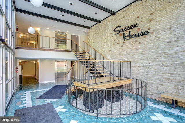 stairs featuring a high ceiling, tile patterned floors, brick wall, baseboards, and beamed ceiling