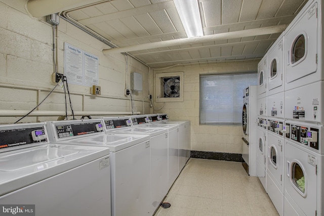 community laundry room featuring stacked washer / dryer, concrete block wall, washer and clothes dryer, and light floors