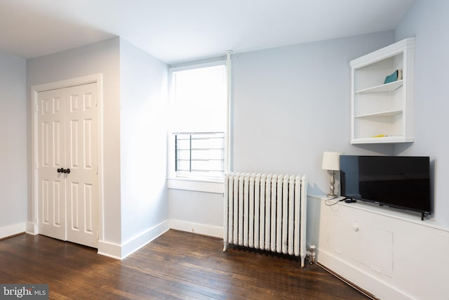 unfurnished bedroom with baseboards, radiator heating unit, wood finished floors, and a closet