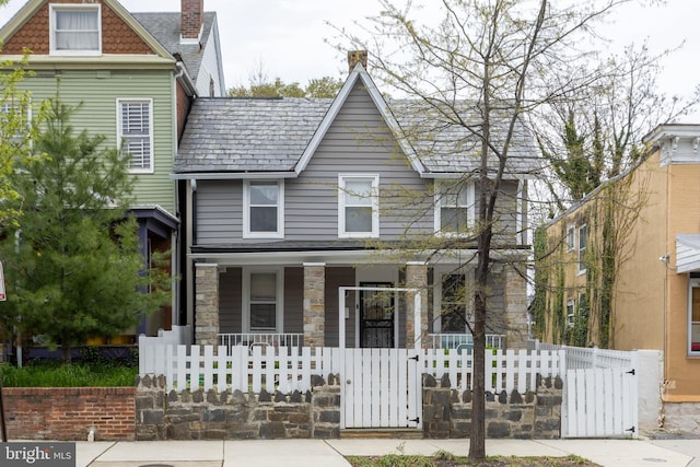 view of front facade featuring a gate, a fenced front yard, stone siding, and covered porch