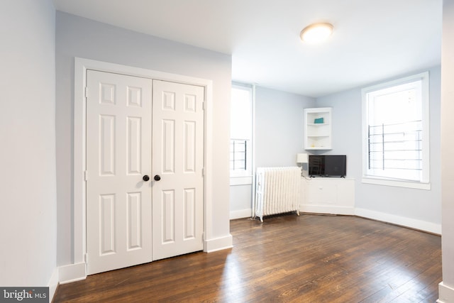 unfurnished bedroom featuring baseboards, dark wood-type flooring, a closet, and radiator