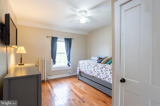 bedroom featuring light wood-type flooring, a ceiling fan, baseboards, and radiator