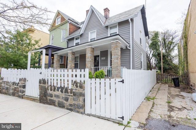 view of front of house with a fenced front yard, a gate, a porch, stone siding, and a chimney