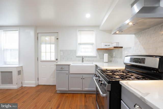 kitchen with wall chimney exhaust hood, a sink, stainless steel gas range, light wood-style floors, and open shelves