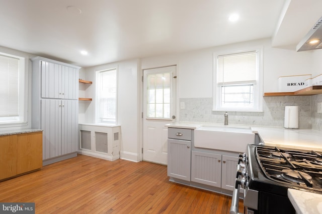 kitchen featuring open shelves, light wood-style flooring, gas stove, and a sink