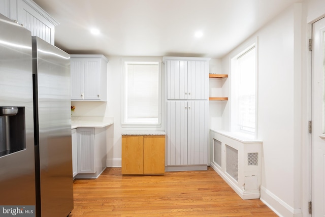 kitchen featuring light countertops, light wood finished floors, stainless steel refrigerator with ice dispenser, and baseboards