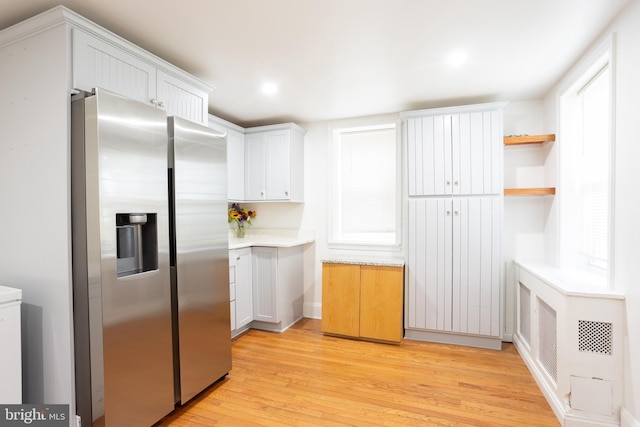 kitchen featuring light wood finished floors, stainless steel fridge, white cabinetry, open shelves, and light countertops