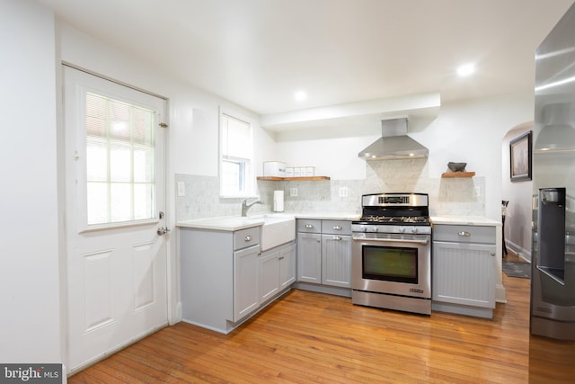 kitchen featuring wall chimney exhaust hood, open shelves, gray cabinetry, and stainless steel gas range oven