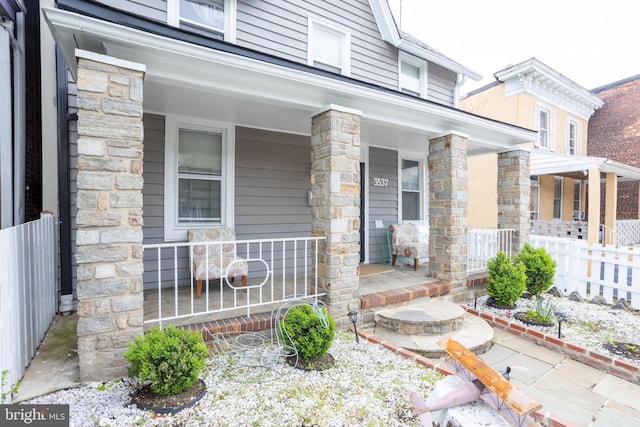 entrance to property featuring stone siding, fence, and covered porch
