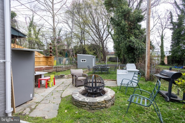 view of yard featuring a storage unit, fence, an outdoor structure, a patio, and an outdoor fire pit
