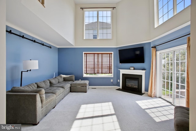 carpeted living area featuring a fireplace with flush hearth, a wealth of natural light, and a towering ceiling