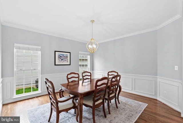 dining area with a notable chandelier, ornamental molding, wood finished floors, and a wainscoted wall