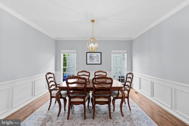 dining area with an inviting chandelier, ornamental molding, light wood-style flooring, and a wainscoted wall