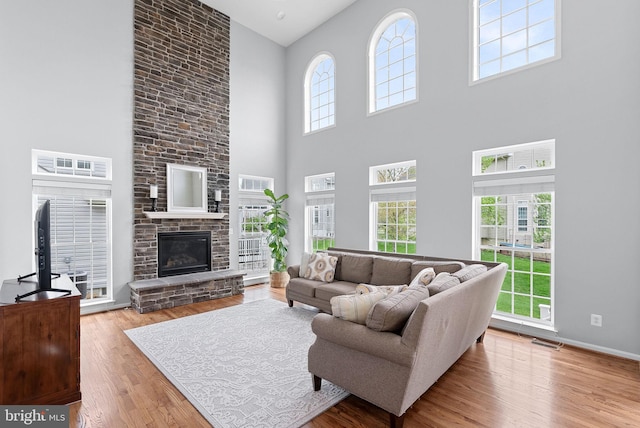 living area featuring visible vents, a high ceiling, a stone fireplace, and wood finished floors
