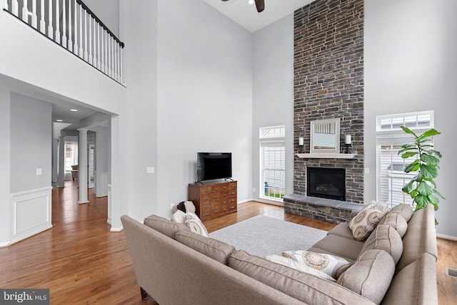 living area with wood finished floors, a ceiling fan, a high ceiling, and a fireplace