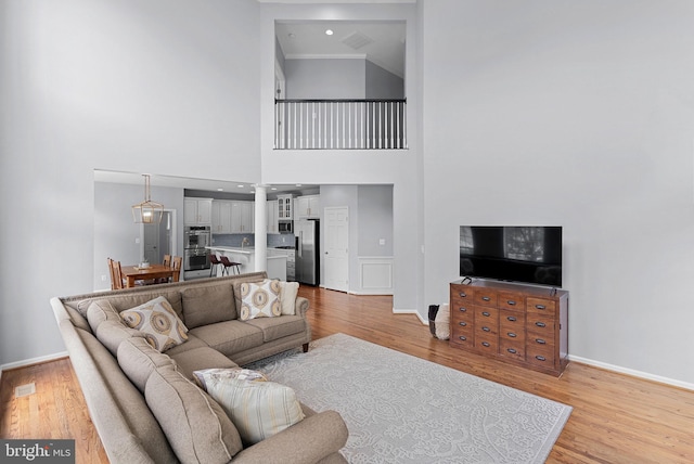 living area featuring a towering ceiling, baseboards, decorative columns, and light wood-style floors