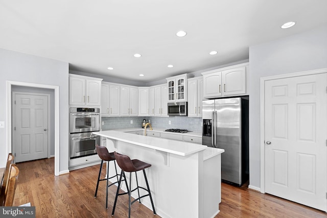kitchen featuring backsplash, appliances with stainless steel finishes, wood finished floors, a breakfast bar, and white cabinetry