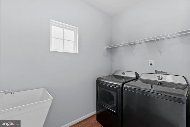 clothes washing area with laundry area, washing machine and dryer, wood finished floors, baseboards, and a sink