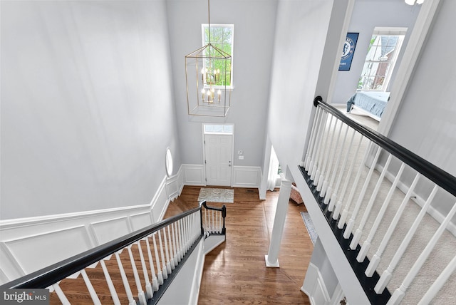 staircase featuring an inviting chandelier, a wainscoted wall, a decorative wall, and wood finished floors
