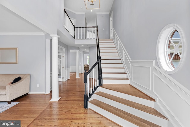 entryway with stairs, light wood-style floors, a high ceiling, a decorative wall, and ornate columns