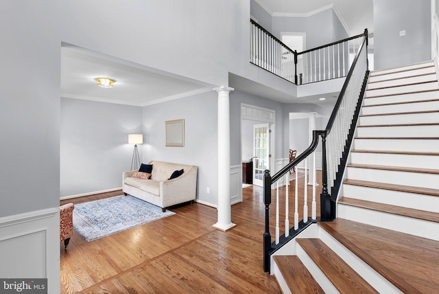 entryway featuring decorative columns, ornamental molding, wood finished floors, and stairway