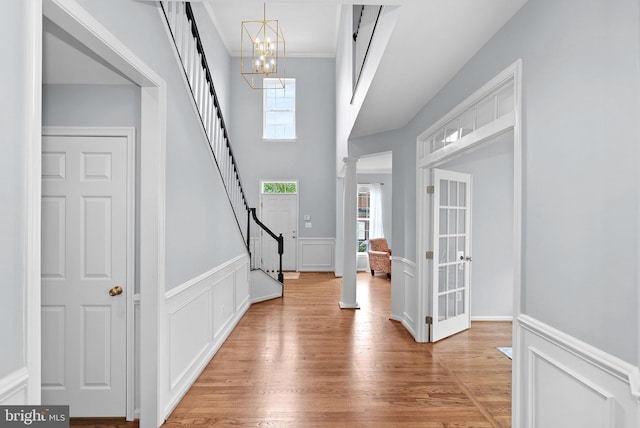 entrance foyer with light wood-style floors, a wainscoted wall, an inviting chandelier, a decorative wall, and stairs