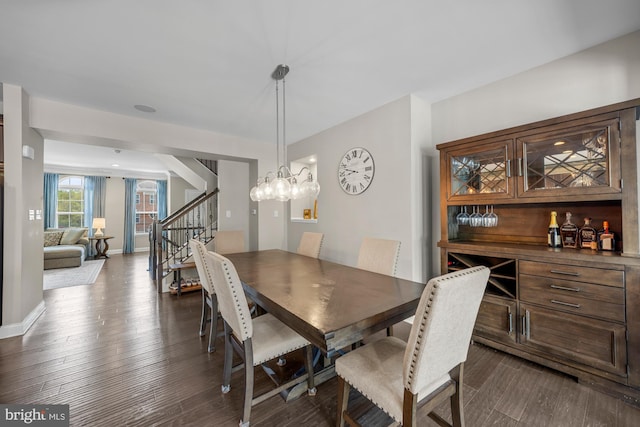 dining space with dark wood-type flooring, stairs, baseboards, and a notable chandelier