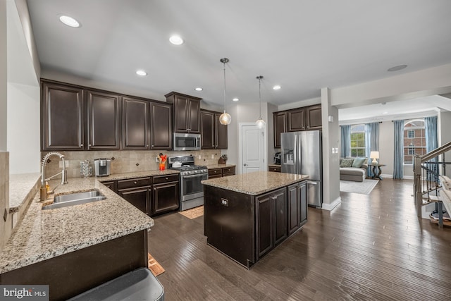 kitchen featuring decorative backsplash, appliances with stainless steel finishes, dark brown cabinets, a sink, and light stone counters