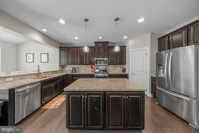 kitchen featuring appliances with stainless steel finishes, a sink, a center island, tasteful backsplash, and dark wood-type flooring