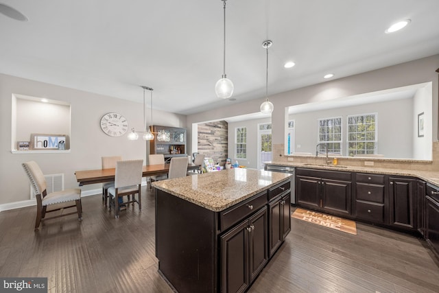 kitchen featuring dark wood-style flooring, decorative light fixtures, stainless steel dishwasher, a sink, and light stone counters