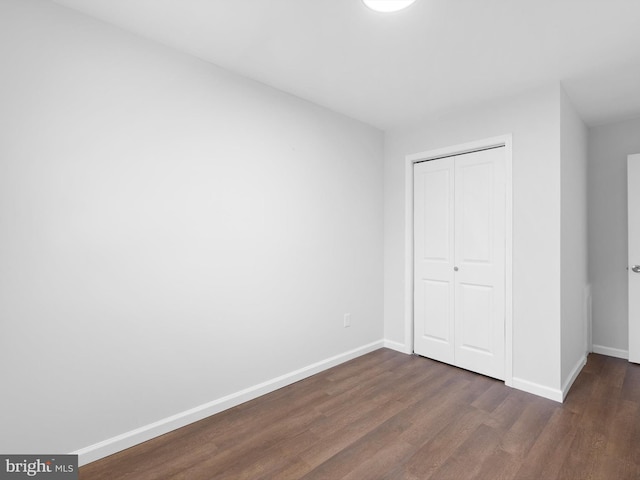 unfurnished bedroom with baseboards, dark wood-type flooring, and a closet