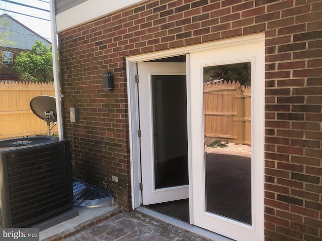 view of exterior entry featuring fence, brick siding, and central air condition unit