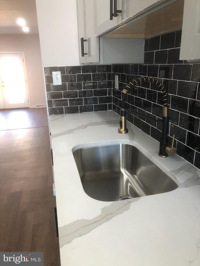 room details featuring wood finished floors, a sink, light stone countertops, tasteful backsplash, and white cabinetry