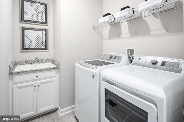 washroom with a sink, baseboards, cabinet space, and separate washer and dryer