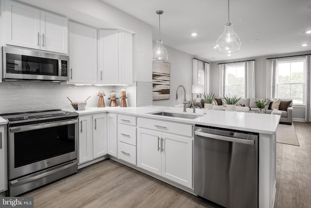 kitchen with open floor plan, a peninsula, light countertops, appliances with stainless steel finishes, and a sink
