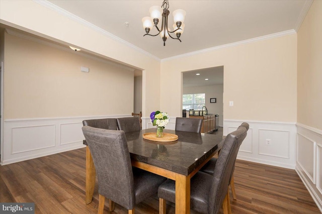 dining room featuring dark wood finished floors, a decorative wall, crown molding, and a chandelier