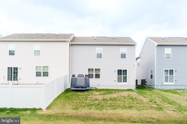 rear view of property featuring fence, a lawn, central AC, and a trampoline