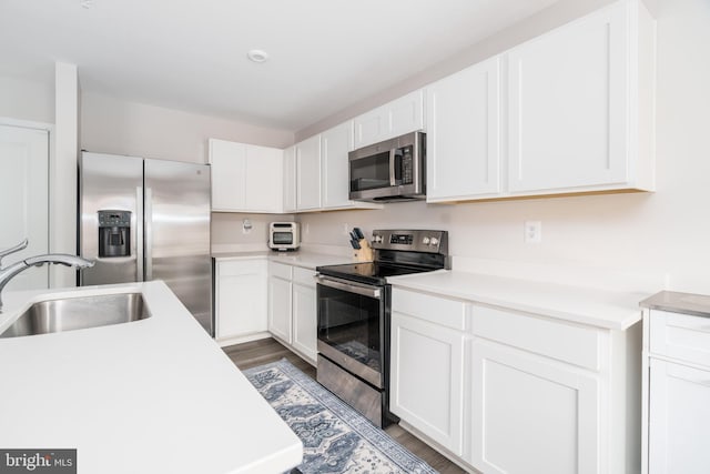 kitchen with white cabinetry, appliances with stainless steel finishes, a sink, and dark wood-style floors