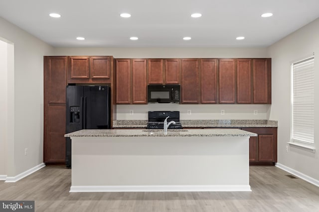 kitchen with an island with sink, light wood-style flooring, baseboards, and black appliances