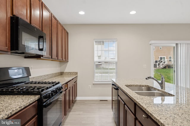 kitchen with light wood-type flooring, recessed lighting, black appliances, light stone countertops, and a sink
