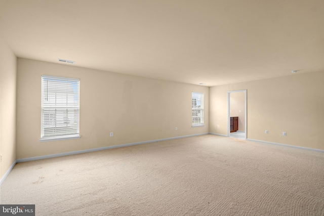 empty room featuring light carpet, a healthy amount of sunlight, baseboards, and visible vents