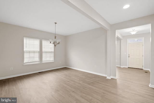 empty room featuring a chandelier, plenty of natural light, light wood-style flooring, and baseboards