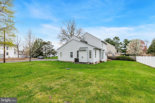 back of property with central AC, fence, and a lawn