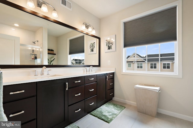 bathroom featuring a stall shower, double vanity, a sink, and baseboards
