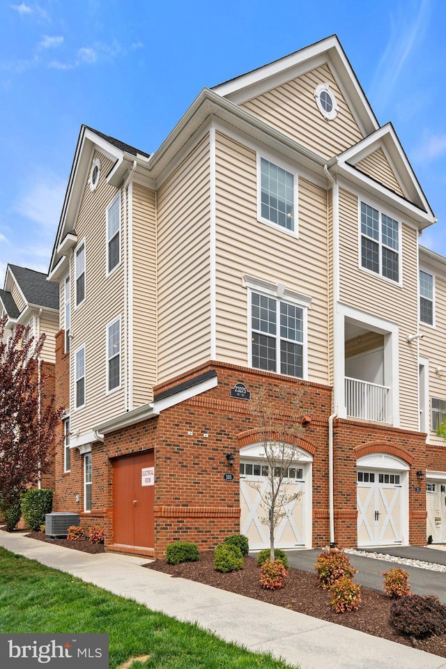 townhome / multi-family property featuring brick siding, a garage, driveway, and central AC