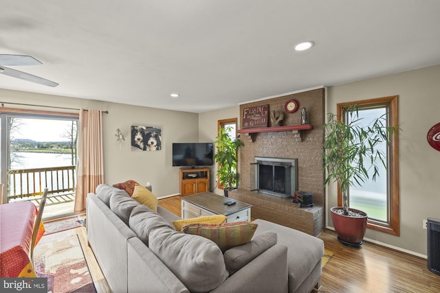 living room featuring a water view, a ceiling fan, a fireplace, and a healthy amount of sunlight