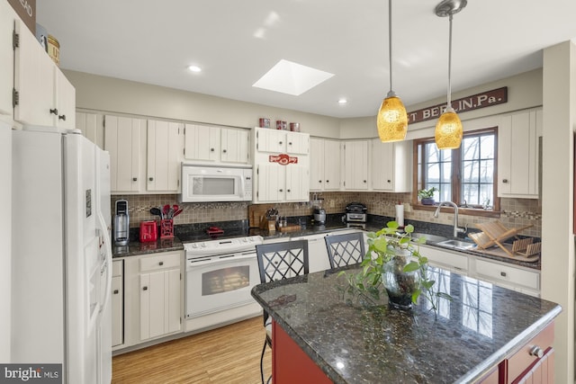 kitchen featuring white appliances, a center island, backsplash, a skylight, and a sink