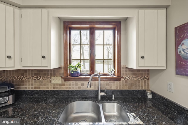 kitchen with backsplash, a sink, white cabinetry, and dark stone countertops