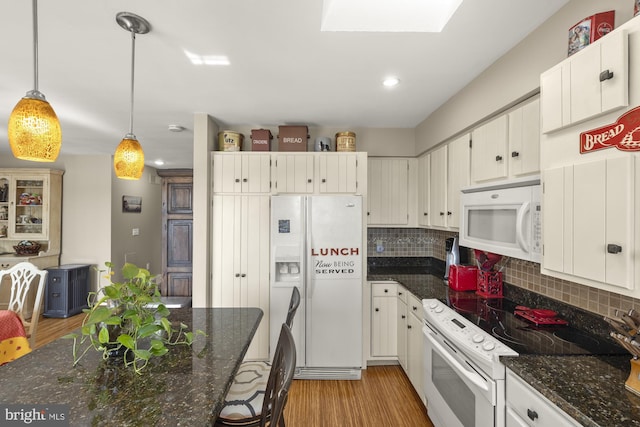 kitchen with light wood-type flooring, dark stone countertops, white appliances, backsplash, and hanging light fixtures