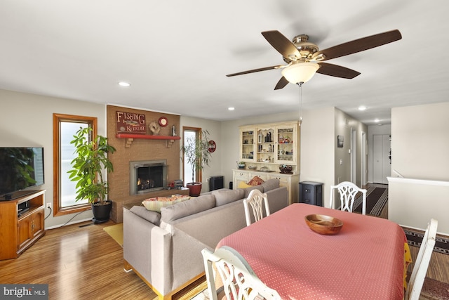 dining space featuring wood finished floors, ceiling fan, a brick fireplace, and a healthy amount of sunlight